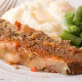 A dinner plate with homestyle Italian meatloaf, mashed potatoes, and green beans.