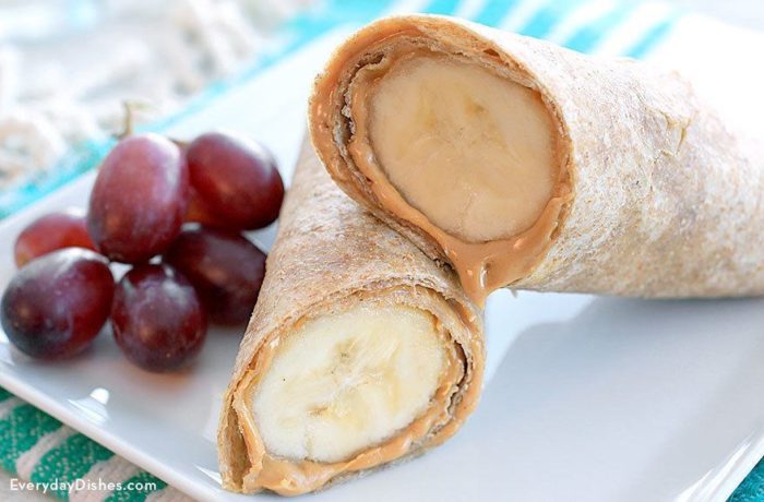 A peanut butter banana wrap, sliced in half with grapes on the side.