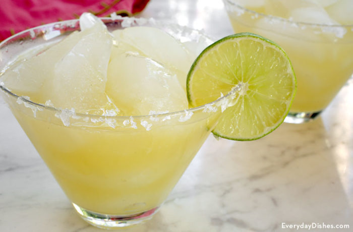 A glass full of a champagne margarita, garnished with lime