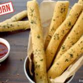 A fresh batch of einkorn chewy breadsticks with a dish of dipping sauce.