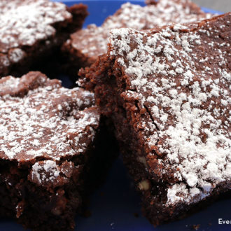 A batch of homemade chewy gluten-free brownies that are dusted with powdered sugar.