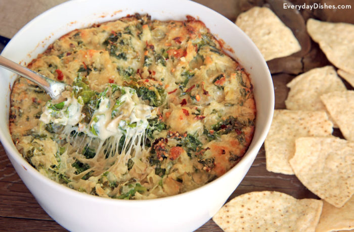 A bowl of homemade kale and artichoke dip with chips to enjoy it.