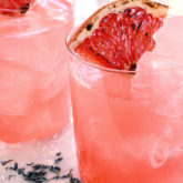 Two refreshing glasses of a blushing whiskey and lavender cocktail, garnished with grapefruit