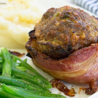 A bacon-wrapped mini meatloaf cup on a plate with mashed potatoes and green beans