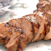 A grilled pork tenderloin, sliced on a plate and ready to have for dinner.