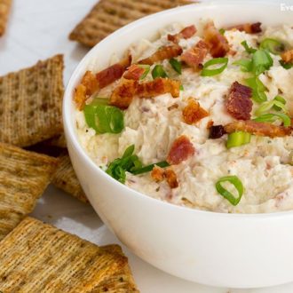 A bowl of bacon white cheddar dip, next to some crackers.