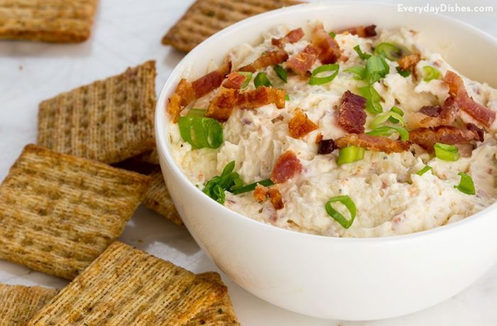 A bowl of bacon white cheddar dip, next to some crackers.