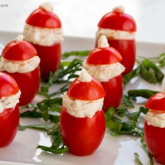 A plate of bite-sized stuffed tomatoes decorated like Santa