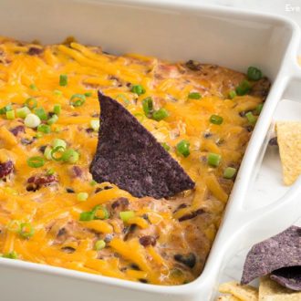 A pan of homemade gooey bean dip with a chip dipped into it.
