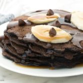 A short stack of chocolate pancakes that are topped with bananas and syrup.