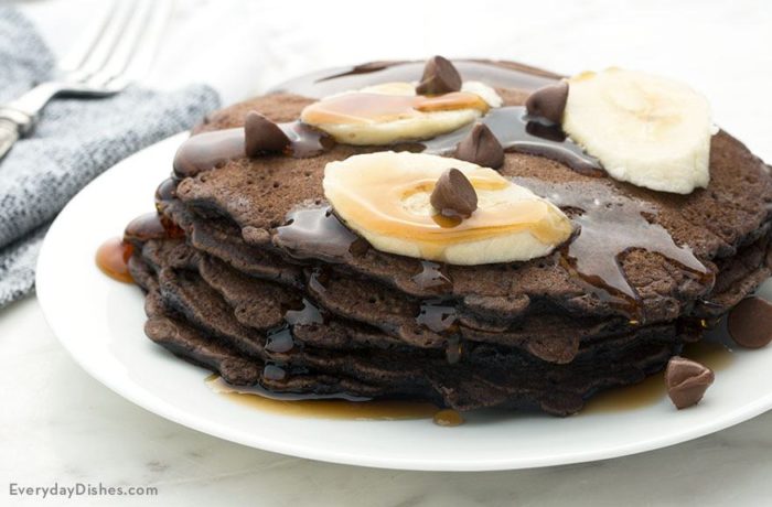 A short stack of chocolate pancakes that are topped with bananas and syrup.