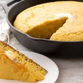 A batch of homemade einkorn skillet cornbread, with a slice cut out and topped with butter.