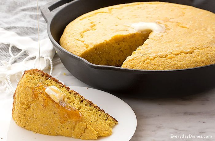 A batch of homemade einkorn skillet cornbread, with a slice cut out and topped with butter.