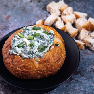 A bread bowl full of homemade spinach dip, ready to serve as an appetizer
