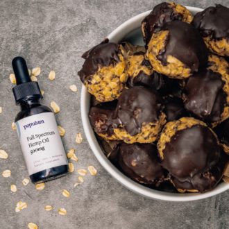 A bowl of CBD oil protein balls next to a bottle of Populum hemp oil.