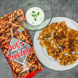A plate of homemade chicken tenders, next to a bowl of dipping sauce and a bag of Dot's Pretzels, which were used as breading on the tenders.