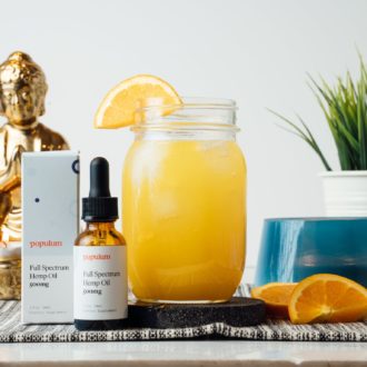 A populum CBD mocktail in a mason jar, garnished with an orange slice, next to more slices and the populum product.