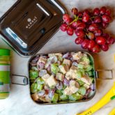 A pan of Whole 30 chick salad, with a jar of avocado oil, fresh grapes, and lemon.