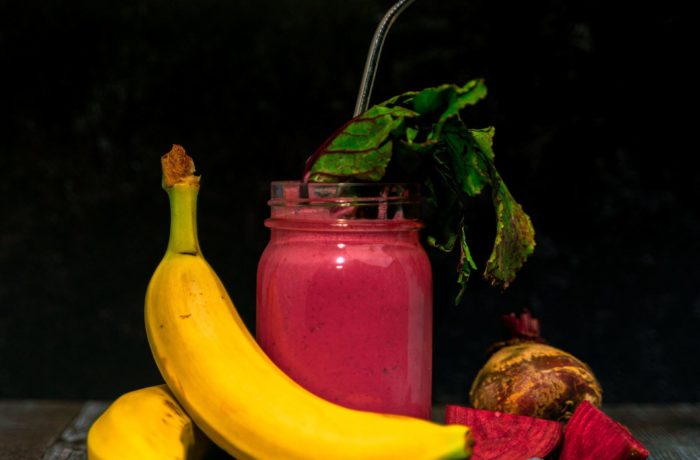 A heart beet smoothie in a mason jar, ready to enjoy, and surrounded by beets, bananas, and blueberries.