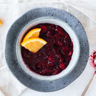A bowl of delicious paleo cranberry sauce, garnished with orange slices.