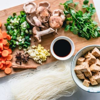 Several healthy, fresh ingredients laid out on a wooden cutting board next to a bowl of tofu.