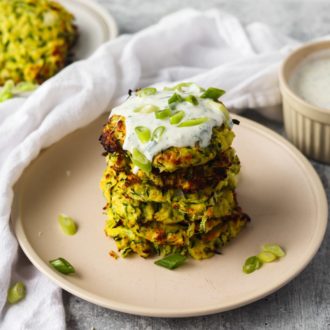 A plate of zucchini fritters topped with yogurt dill sauce
