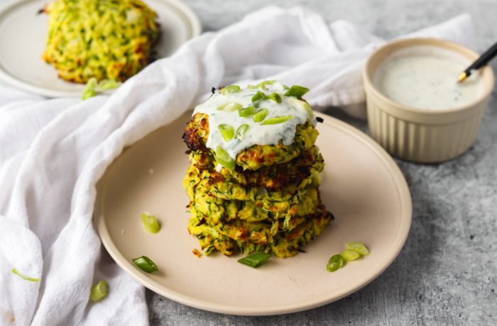 A plate of zucchini fritters topped with yogurt dill sauce