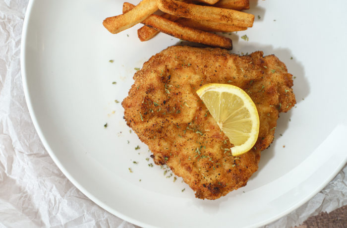 A plate of schnitzel, made in the air fryer, with fries and garnished with a lemon wedge.
