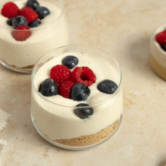 Four jars of high protein cheesecake cups with fresh berries on a white countertop.
