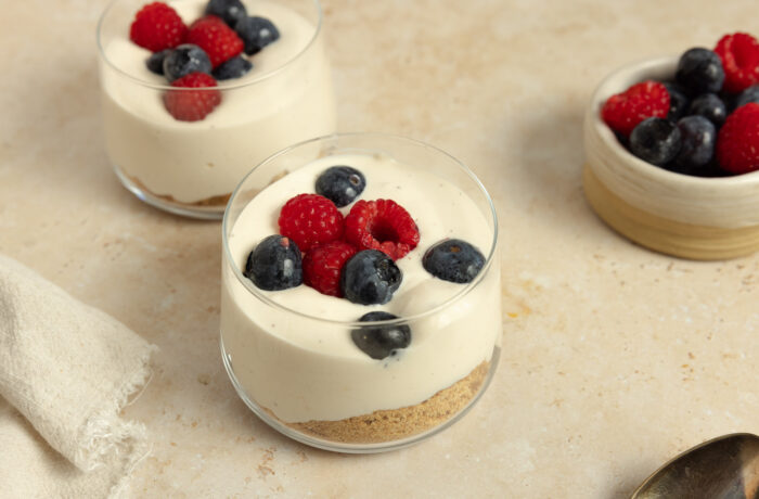 Four jars of high protein cheesecake cups with fresh berries on a white countertop.